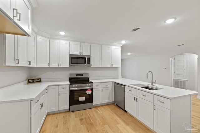 kitchen with light wood finished floors, visible vents, a peninsula, stainless steel appliances, and a sink