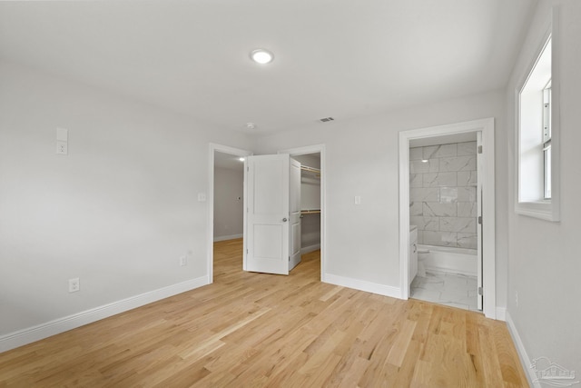 unfurnished bedroom with light wood finished floors, visible vents, a walk in closet, and baseboards