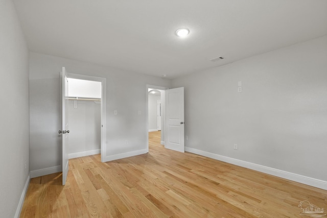 unfurnished bedroom with a spacious closet, visible vents, baseboards, light wood-type flooring, and a closet