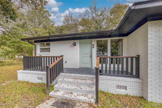 entrance to property featuring crawl space, covered porch, and brick siding