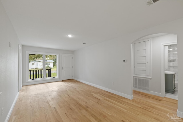 empty room featuring baseboards, visible vents, arched walkways, and light wood-type flooring