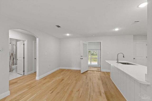 interior space with light wood-type flooring, visible vents, arched walkways, and a sink