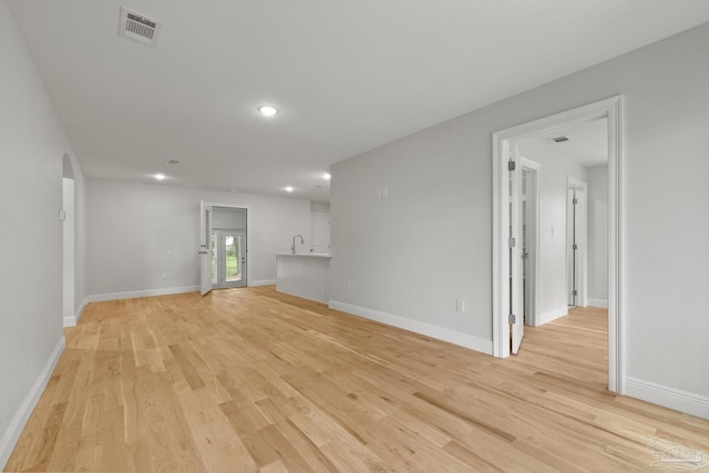 unfurnished living room with light wood finished floors, visible vents, arched walkways, and baseboards