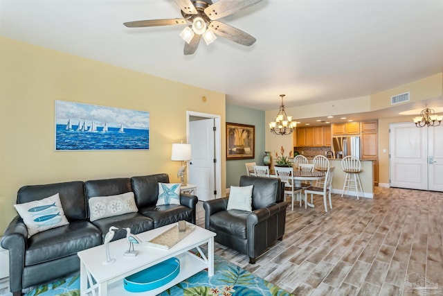 living room with ceiling fan with notable chandelier and light hardwood / wood-style flooring