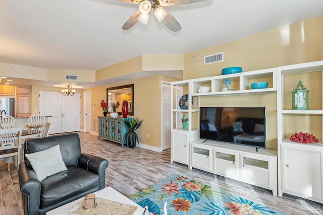 living room featuring ceiling fan with notable chandelier and light hardwood / wood-style flooring