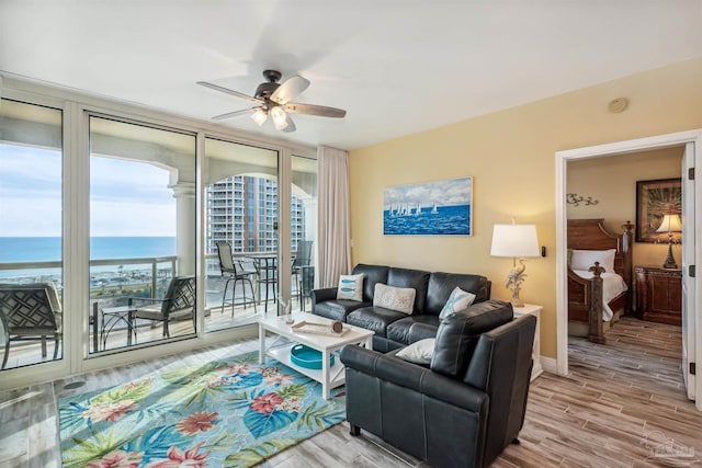 living room with a water view, ceiling fan, floor to ceiling windows, and light hardwood / wood-style floors