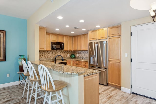 kitchen featuring a breakfast bar, backsplash, stainless steel refrigerator with ice dispenser, light stone countertops, and kitchen peninsula