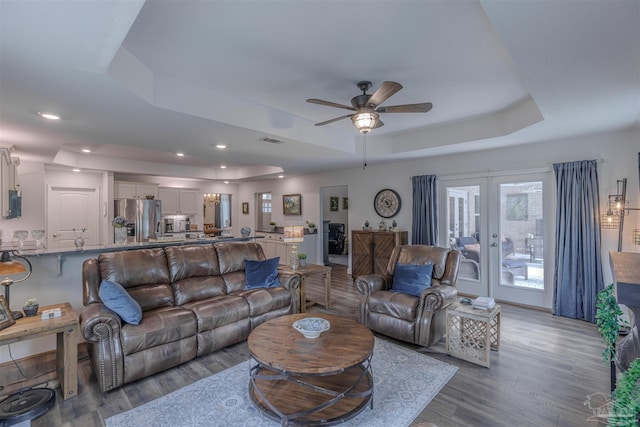 living area with french doors, a ceiling fan, a raised ceiling, and wood finished floors