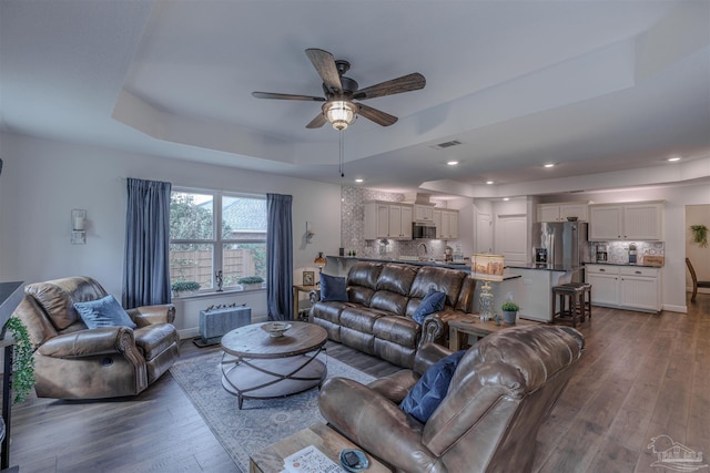 living area with ceiling fan, a raised ceiling, recessed lighting, dark wood-type flooring, and visible vents