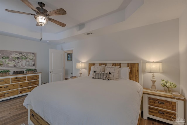 bedroom featuring a ceiling fan, visible vents, wood finished floors, and a raised ceiling