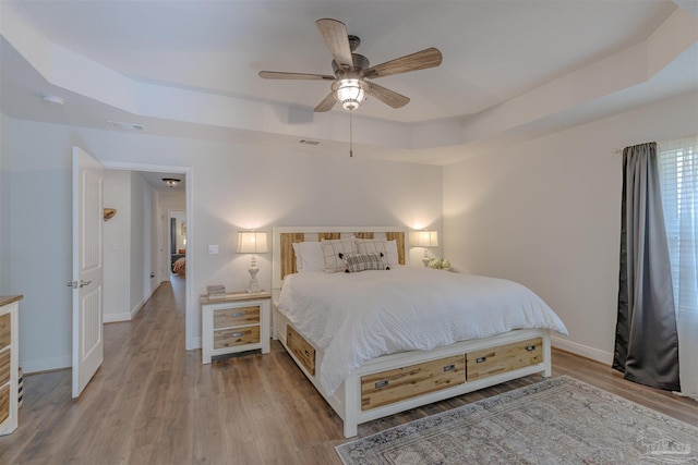 bedroom featuring a raised ceiling, baseboards, wood finished floors, and visible vents