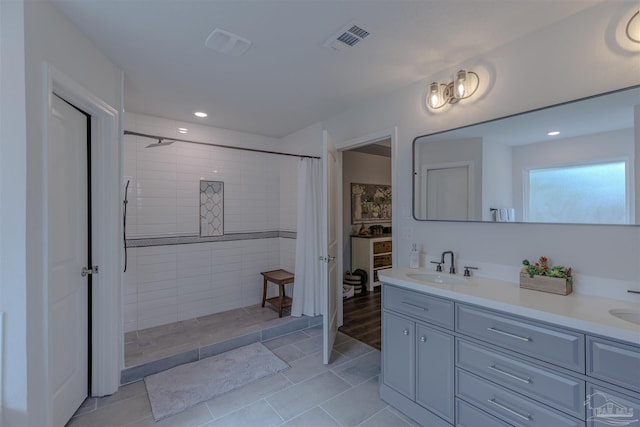 bathroom with a sink, tile patterned flooring, double vanity, visible vents, and tiled shower