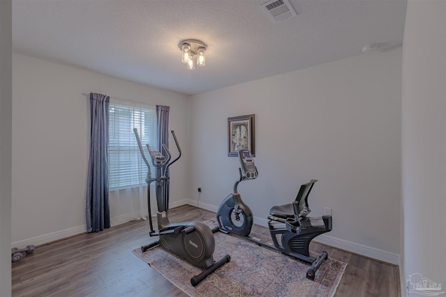 workout area with baseboards, visible vents, and wood finished floors