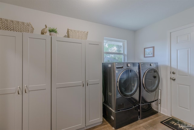 clothes washing area featuring light wood-style floors, cabinet space, and washer and clothes dryer