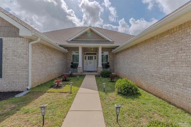 entrance to property featuring a lawn, brick siding, a shingled roof, and a porch