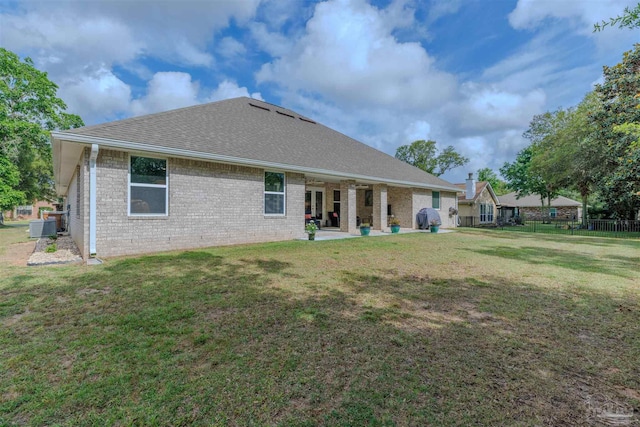 back of house featuring roof with shingles, a lawn, central AC, and brick siding