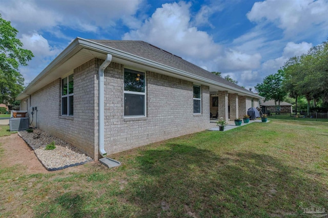 view of property exterior featuring central AC, fence, brick siding, a shingled roof, and a yard