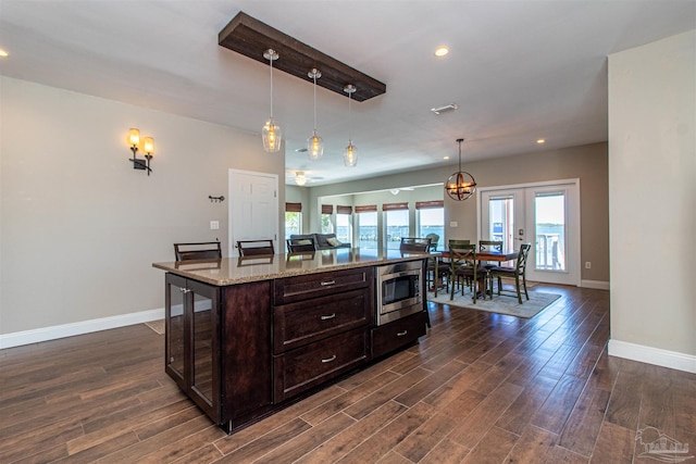 kitchen with hanging light fixtures, dark brown cabinetry, stainless steel microwave, baseboards, and dark wood-style floors