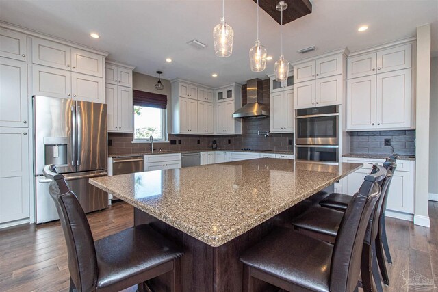 kitchen with tasteful backsplash, wall chimney range hood, dark hardwood / wood-style flooring, a kitchen island, and appliances with stainless steel finishes