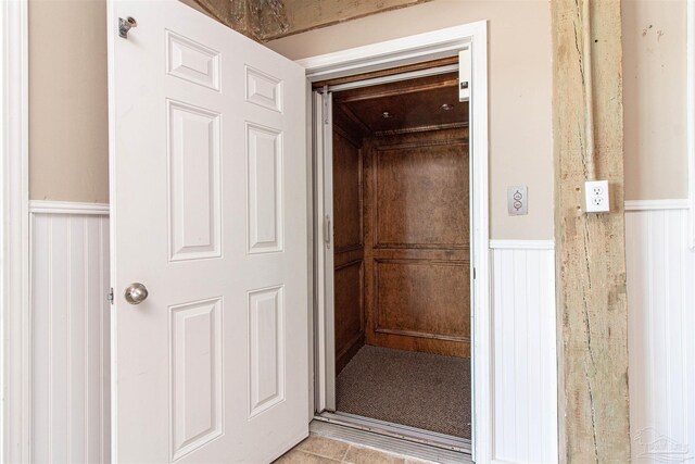 interior space with wainscoting, elevator, tile patterned flooring, and a decorative wall