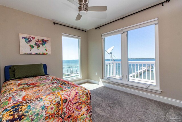 carpeted bedroom featuring ceiling fan, baseboards, multiple windows, and a water view