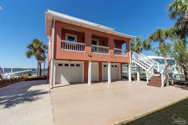 beach home featuring concrete driveway, covered porch, stairs, and a garage