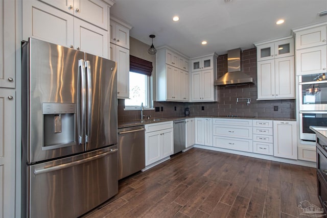 kitchen featuring a sink, glass insert cabinets, stainless steel appliances, wall chimney exhaust hood, and dark wood-type flooring