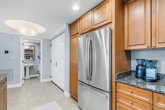 kitchen with stainless steel refrigerator, sink, dark stone counters, ornamental molding, and light tile patterned floors