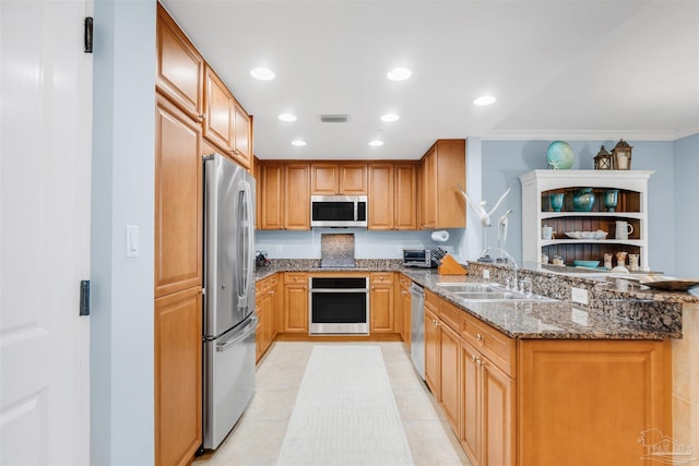 kitchen with sink, light tile patterned floors, appliances with stainless steel finishes, dark stone countertops, and kitchen peninsula