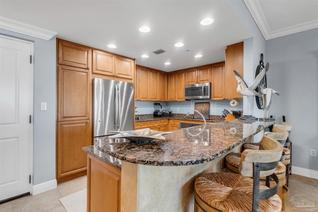 kitchen with stainless steel appliances, crown molding, a breakfast bar, and dark stone counters