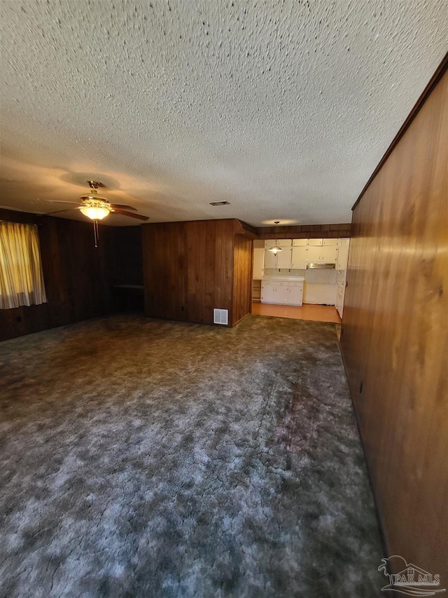 interior space with visible vents, a textured ceiling, wooden walls, carpet flooring, and ceiling fan