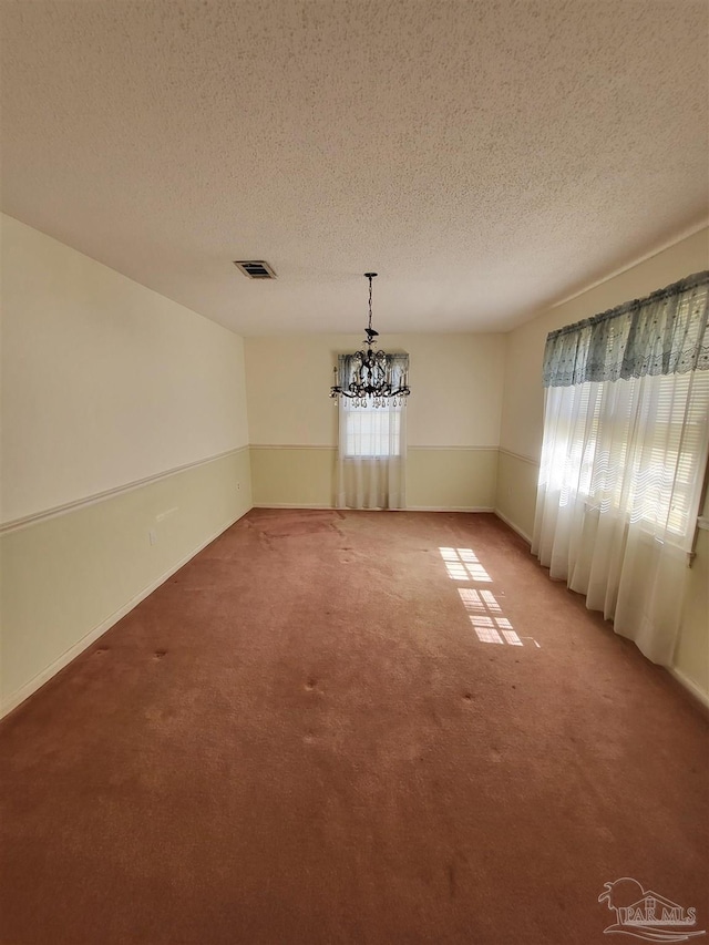 unfurnished dining area featuring a notable chandelier, visible vents, light colored carpet, and a textured ceiling