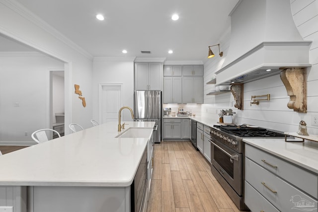 kitchen featuring a large island with sink, custom exhaust hood, stainless steel appliances, and light wood-type flooring