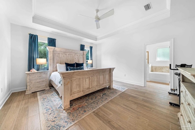 bedroom featuring multiple windows, ensuite bathroom, light wood-type flooring, and a raised ceiling