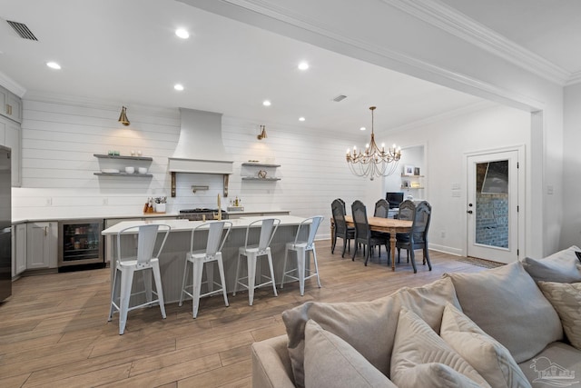 kitchen with premium range hood, a breakfast bar area, light wood-type flooring, and beverage cooler