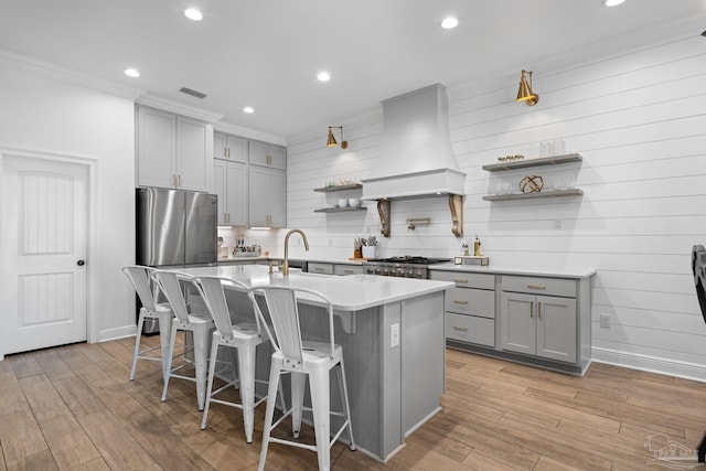 kitchen featuring light hardwood / wood-style floors, gray cabinets, custom range hood, a breakfast bar, and a center island with sink