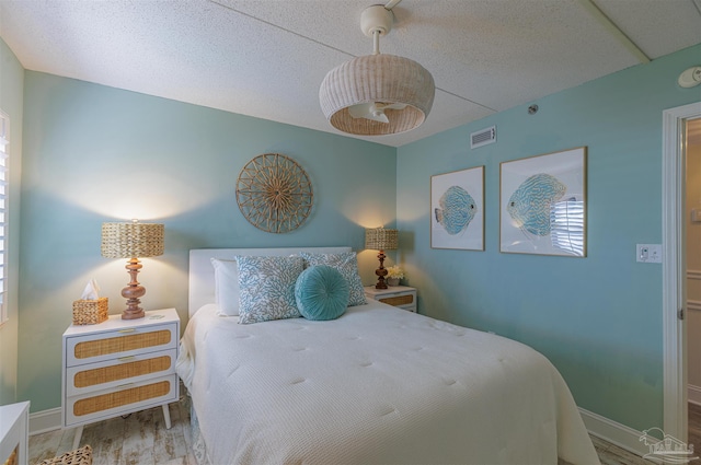 bedroom featuring a textured ceiling, wood finished floors, visible vents, and baseboards