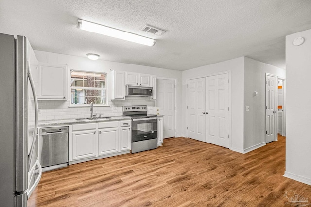 kitchen featuring stainless steel appliances, white cabinetry, sink, tasteful backsplash, and light hardwood / wood-style flooring