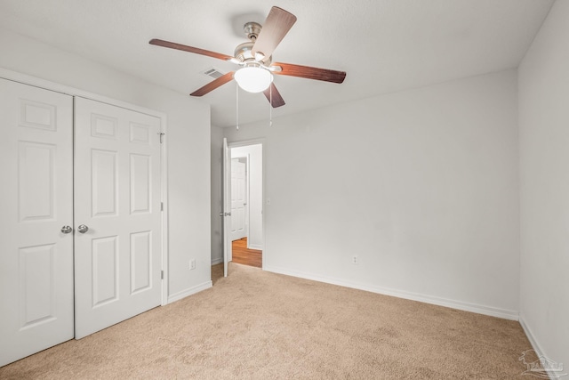 unfurnished bedroom with ceiling fan, light carpet, and a closet