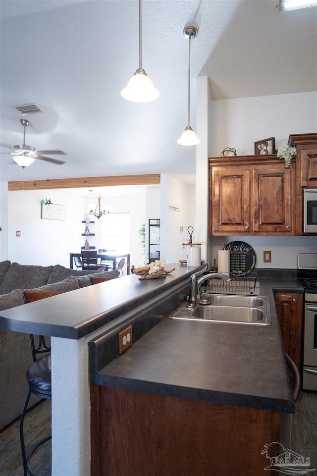 kitchen with ceiling fan, appliances with stainless steel finishes, a kitchen breakfast bar, dark wood-type flooring, and sink