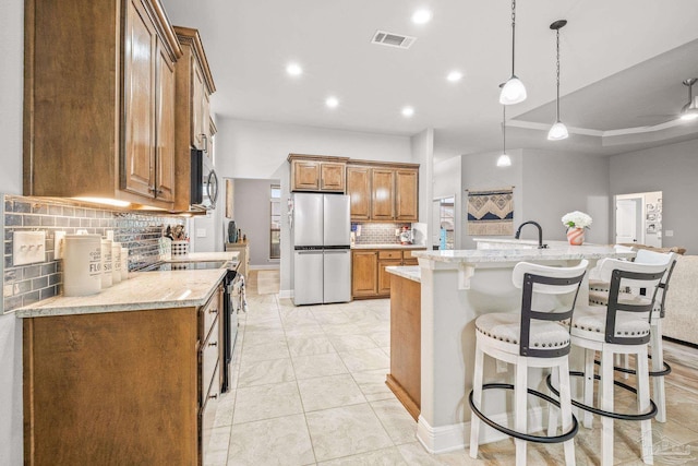 kitchen featuring light stone counters, hanging light fixtures, a center island with sink, a tray ceiling, and stainless steel appliances