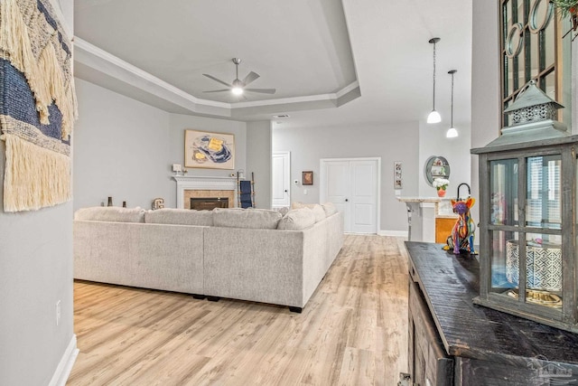 living room featuring crown molding, light hardwood / wood-style flooring, ceiling fan, and a tray ceiling