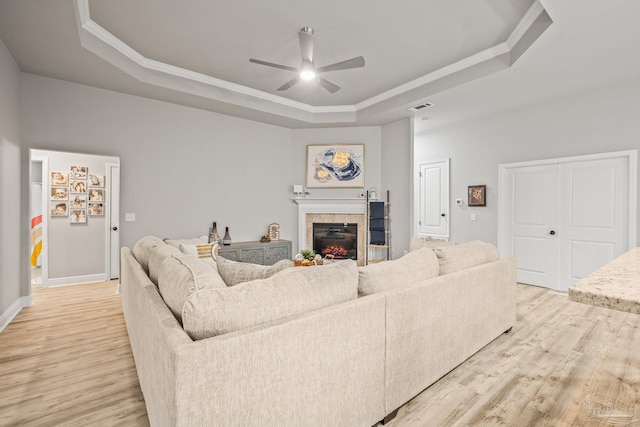 living room with a fireplace, a raised ceiling, ceiling fan, and light wood-type flooring