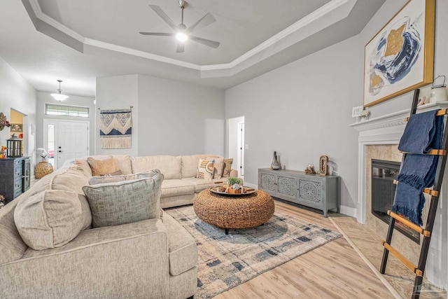 living room featuring a raised ceiling, a tiled fireplace, ornamental molding, and light wood-type flooring