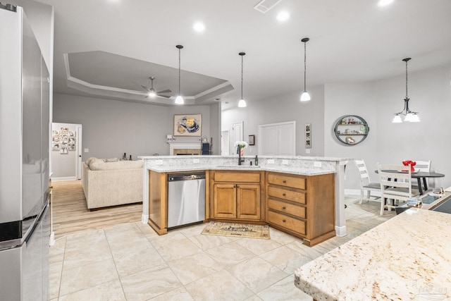 kitchen with sink, hanging light fixtures, a tray ceiling, dishwasher, and a kitchen island with sink