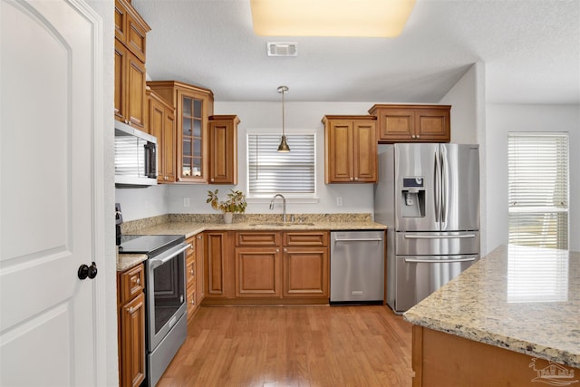949 Osprey Ct, Pensacola, FL 32507 - kitchen featuring stainless steel appliances, a sink, brown cabinets, light wood-style floors, and glass insert cabinets