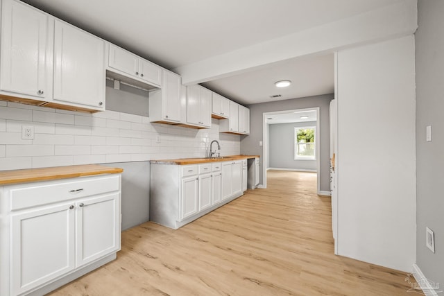 kitchen featuring white cabinetry, butcher block counters, sink, decorative backsplash, and light hardwood / wood-style flooring