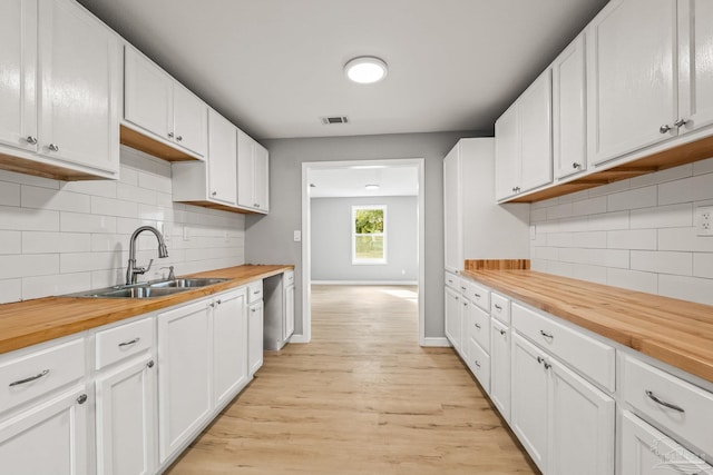 kitchen featuring sink, butcher block countertops, white cabinetry, light wood-type flooring, and decorative backsplash