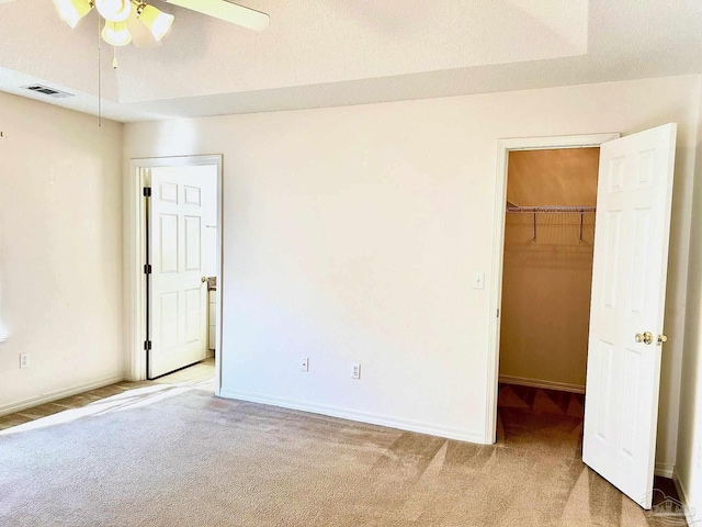 unfurnished bedroom featuring a raised ceiling, a walk in closet, ceiling fan, and carpet