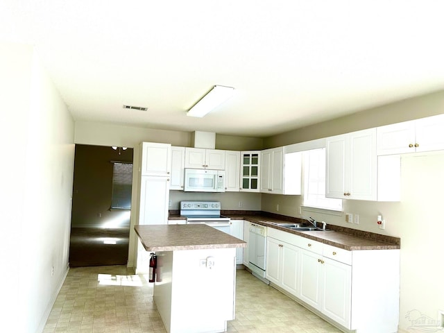 kitchen featuring white appliances, sink, white cabinets, a center island, and a breakfast bar area